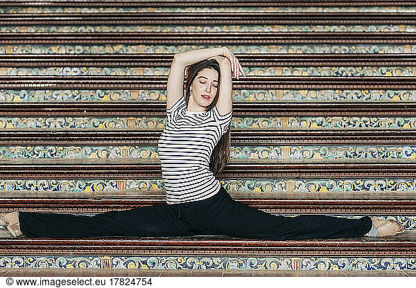 Woman with arms raised doing splits on staircase
