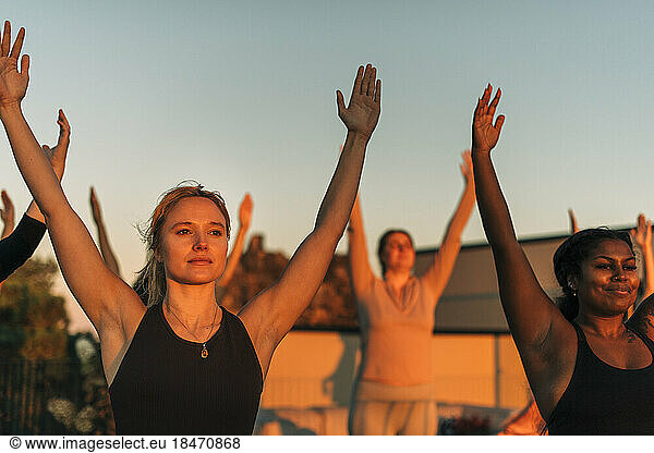 Woman with arms raised exercising with female friend at sunset