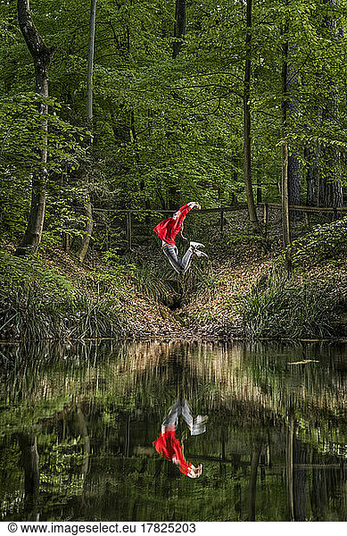 Woman with arms raised jumping by reflection in lake