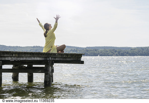 Woman with arms raised sitting on boardwalk at the lake  Ammersee  Upper Bavaria  Germany