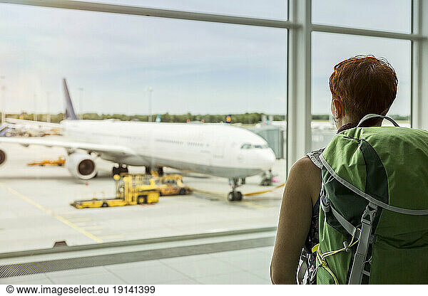 Woman with backpack looking at plane through window at airport