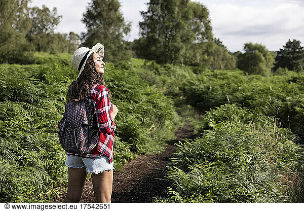 Woman with backpack standing in forest at Cannock Chase on sunny day