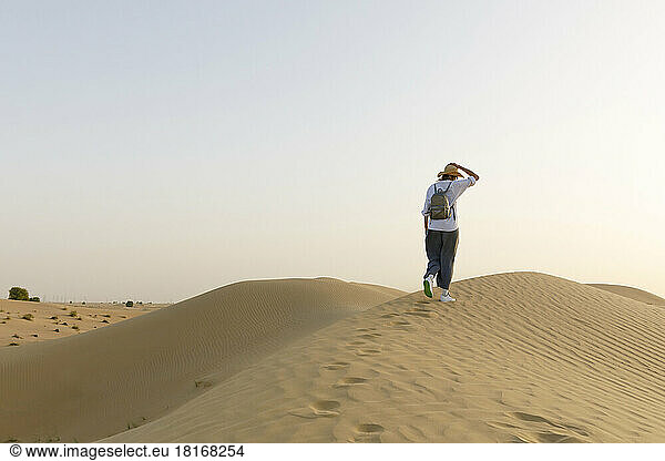Woman with backpack walking on sand dunes in desert