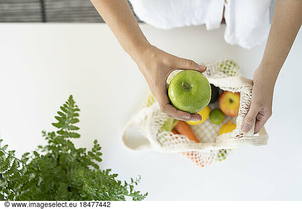 Woman with bag of fresh fruits on table at home