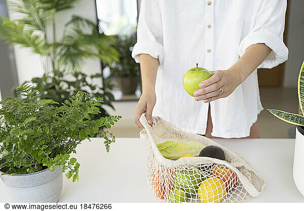 Woman with bag of fruits and vegetables on table at home