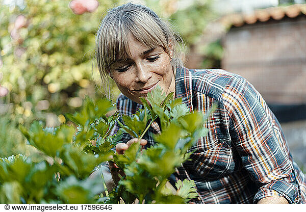 Woman with bangs examining plants in garden