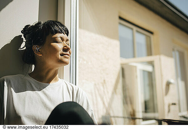 Woman with bangs sitting in sunlight near window at home
