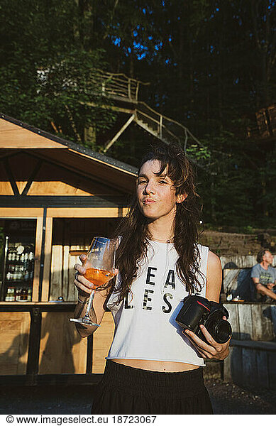 Woman with beverage and camera enjoys summer sun in forrest venue
