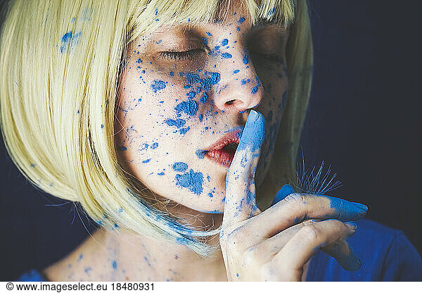 Woman with blue powder paint and finger on lips against black background