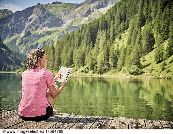 Woman with book day dreaming on jetty by lake