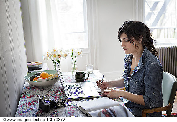 Woman with books and pen using laptop computer for searching recipe