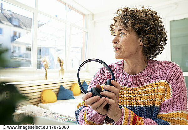 Woman with brown curly hair holding wireless headphones at home
