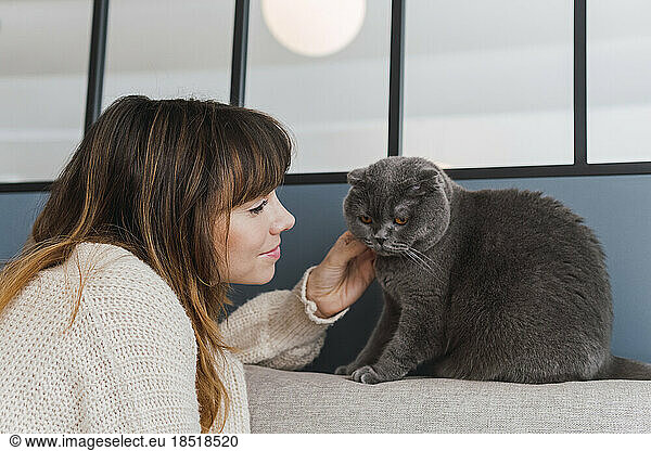 Woman with brown hair stroking cat sitting on sofa at home
