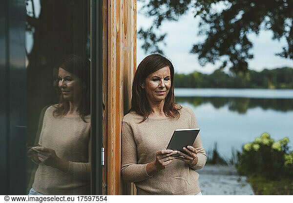 Woman with brown hair using tablet PC by glass wall at backyard