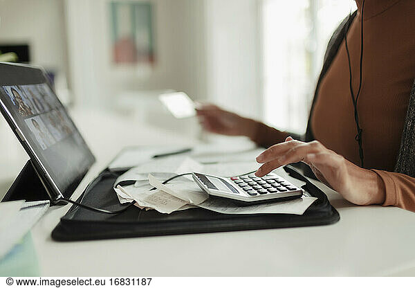 Woman with calculator and receipts paying bills at digital tablet