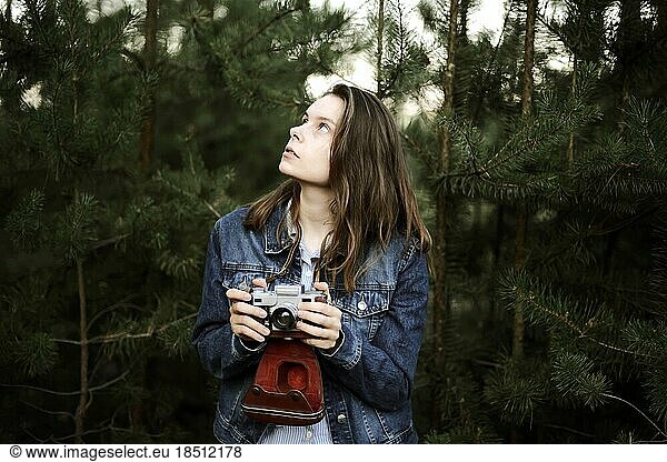 Woman with camera looking away while standing against pine trees