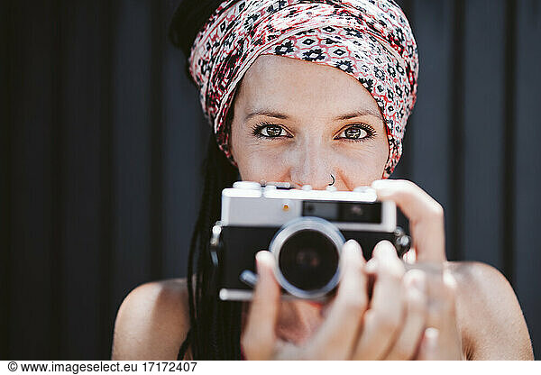 Woman with camera staring while standing against wall