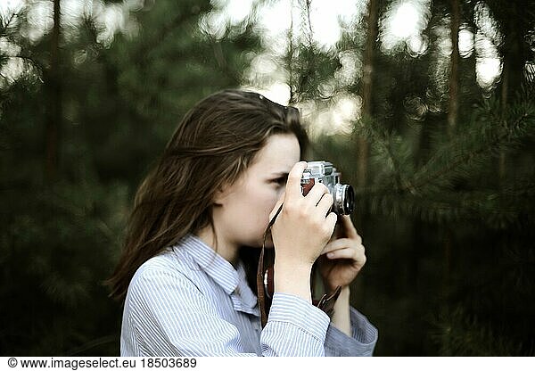 Woman with camera while standing against pine trees