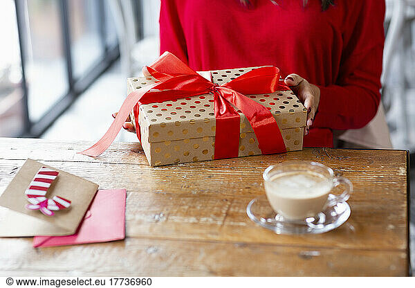 Woman with Christmas present and coffee cup sitting at table in cafe