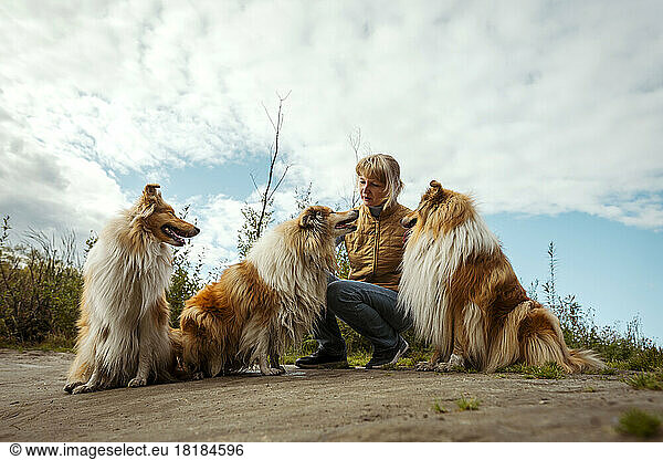 Woman with collie dogs crouching under cloudy sky in nature