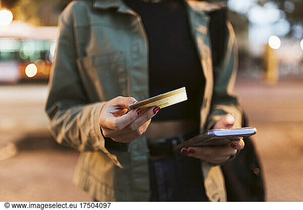 Woman with credit card doing online shopping through mobile phone at night