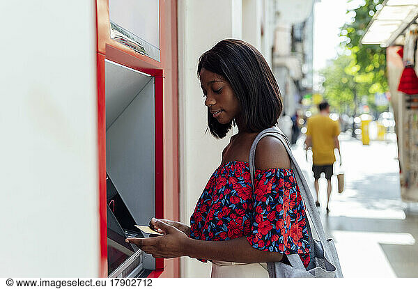 Woman with credit card standing at ATM