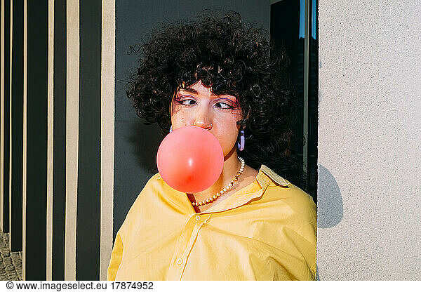 Woman with cross-eyed blowing bubble gum by column