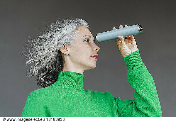 Woman with curly gray hair looking through monocular in front of wall