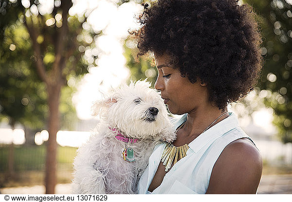 Woman with curly hair kissing dog while standing at park