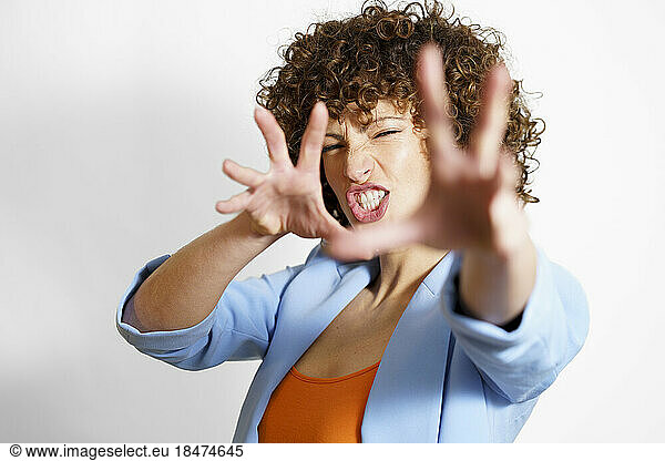 Woman with curly hair making face and gesturing against white background