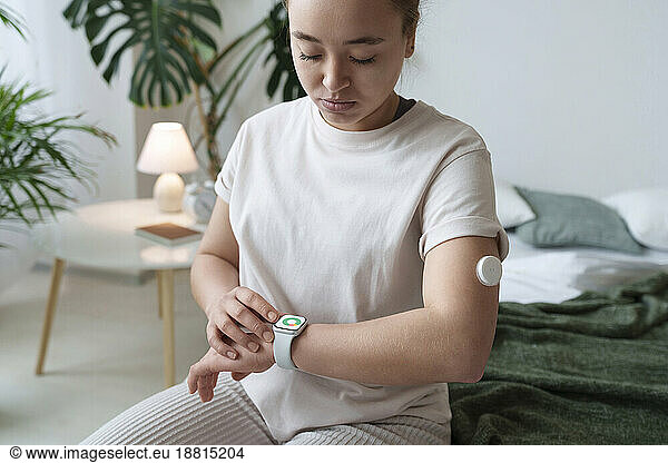 Woman with diabetes checking smart watch sitting on bed at home