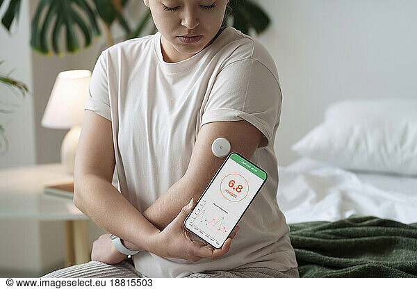 Woman with diabetes synchronizing smart phone with sensor on arm at home