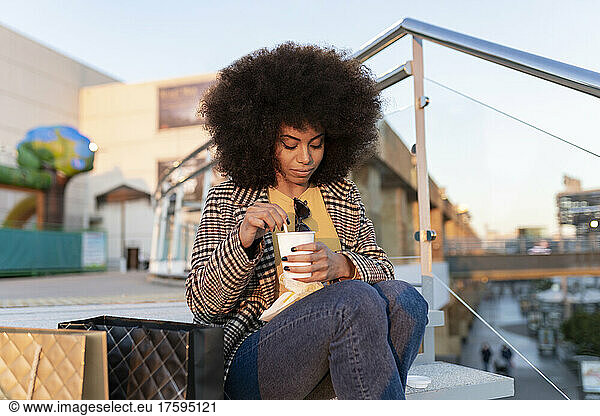 Woman with disposable coffee cup sitting on step