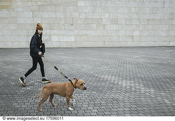 Woman with dog walking on footpath by wall