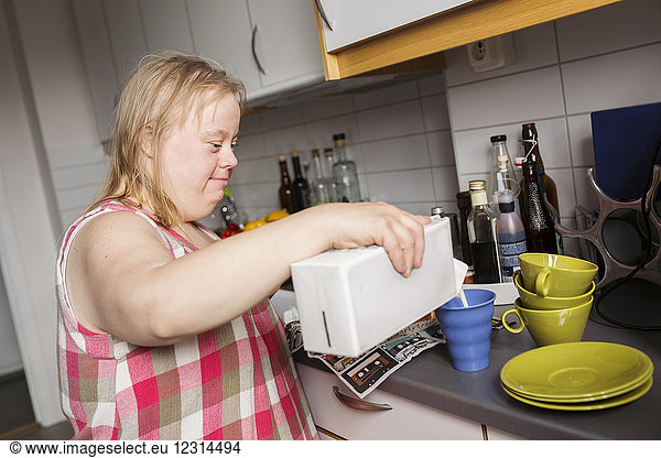 Woman with down syndrome pouring milk to mug in kitchen
