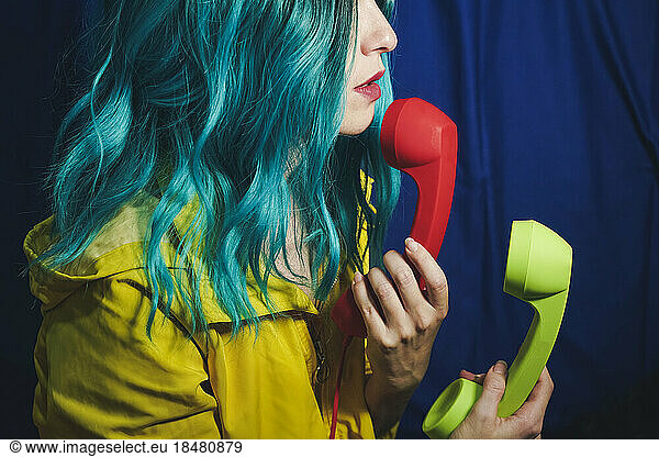 Woman with dyed hair holding red and green telephone receivers in front of blue backdrop