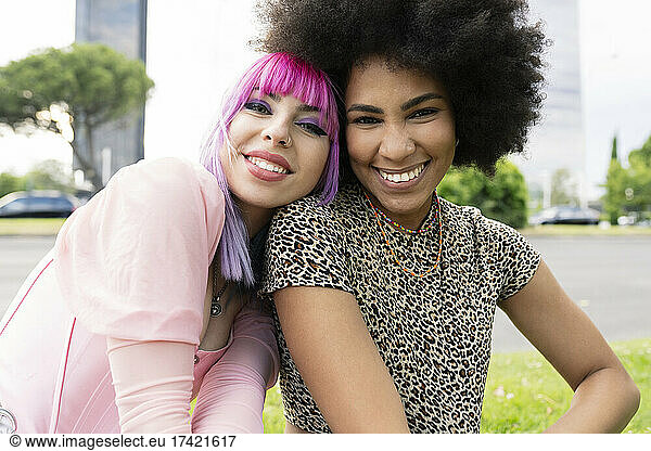 Woman with dyed hair leaning on Afro female friend at park