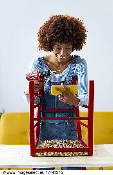 Woman with electric screwdriver using smart phone on table