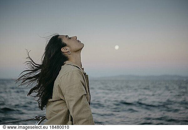 Woman with eyes closed by sea at sunset