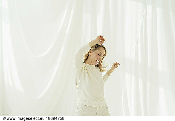 Woman with eyes closed dancing in front of white translucent curtain