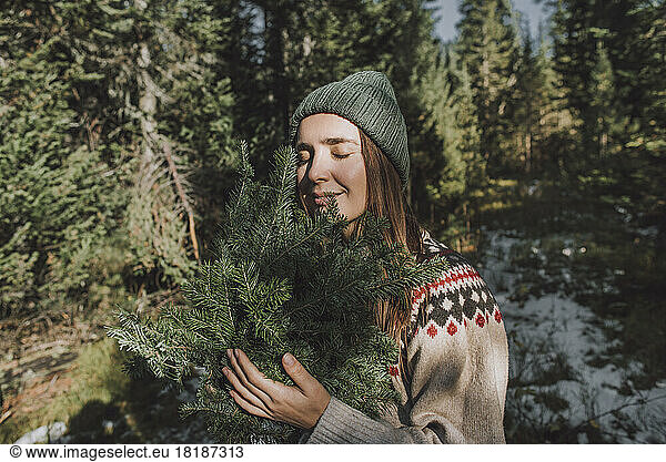 Woman with eyes closed holding twigs of spruce tree