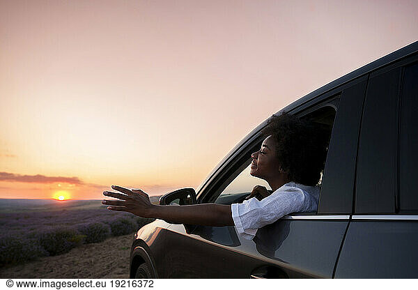 Woman with eyes closed leaning out of car window at sunset