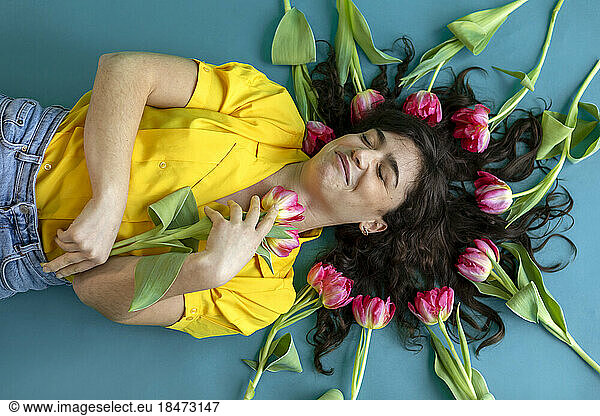 Woman with eyes closed lying down amidst tulips on green background