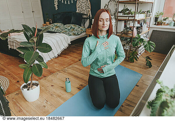 Woman with eyes closed meditating on exercise mat at home
