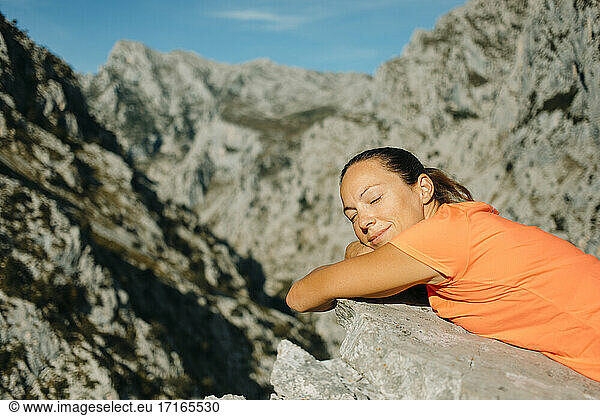 Woman with eyes closed relaxing on rock at Cares Trail in Picos De Europe National Park  Asturias  Spain