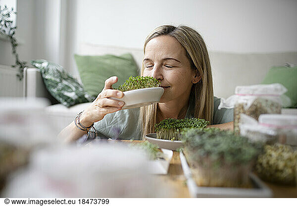 Woman with eyes closed smelling herbs at home