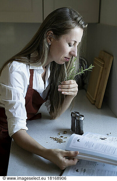 Woman with eyes closed smelling rosemary in kitchen at home