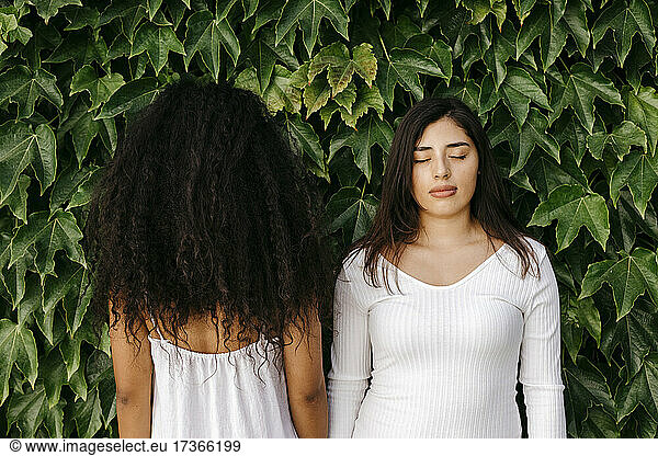 Woman with eyes closed standing near female friend facing plants