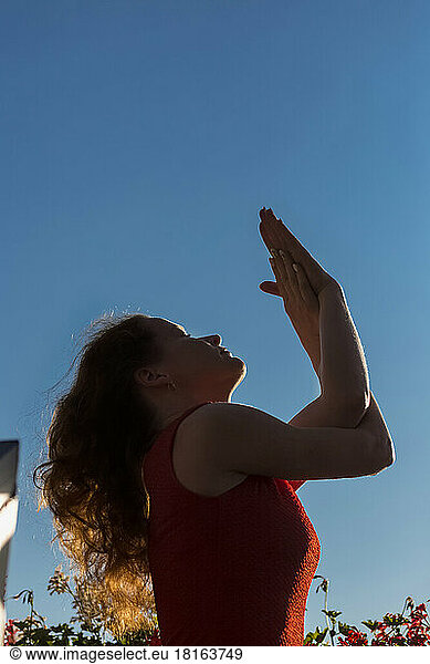 Woman with eyes closed stretching under blue sky