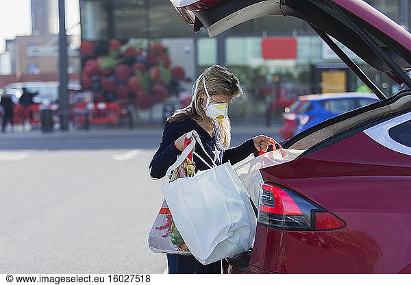 Woman with face mask loading groceries into car in parking lot